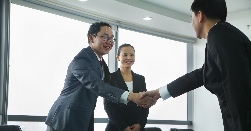 Two Asian corporate men shaking hands over table_C